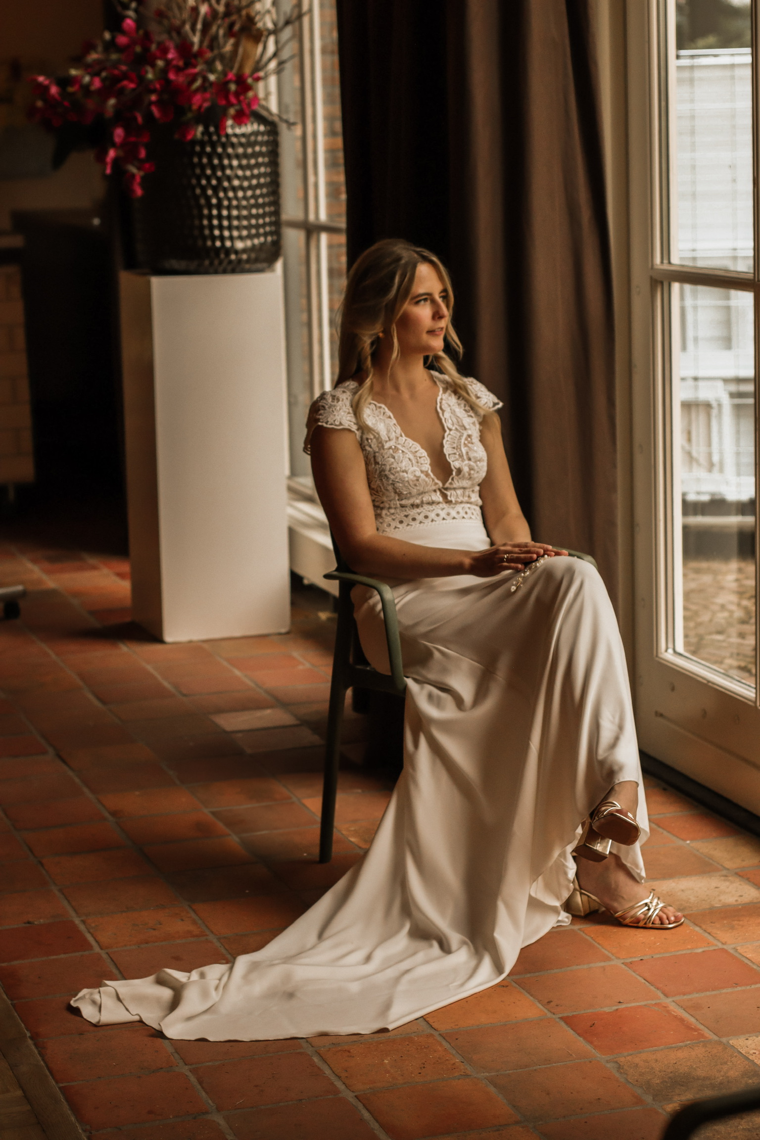 Bruiloft fotografie Haaksbergen - elegante bruid in kanten jurk bij raam door Kim Scharenborg Fotografie