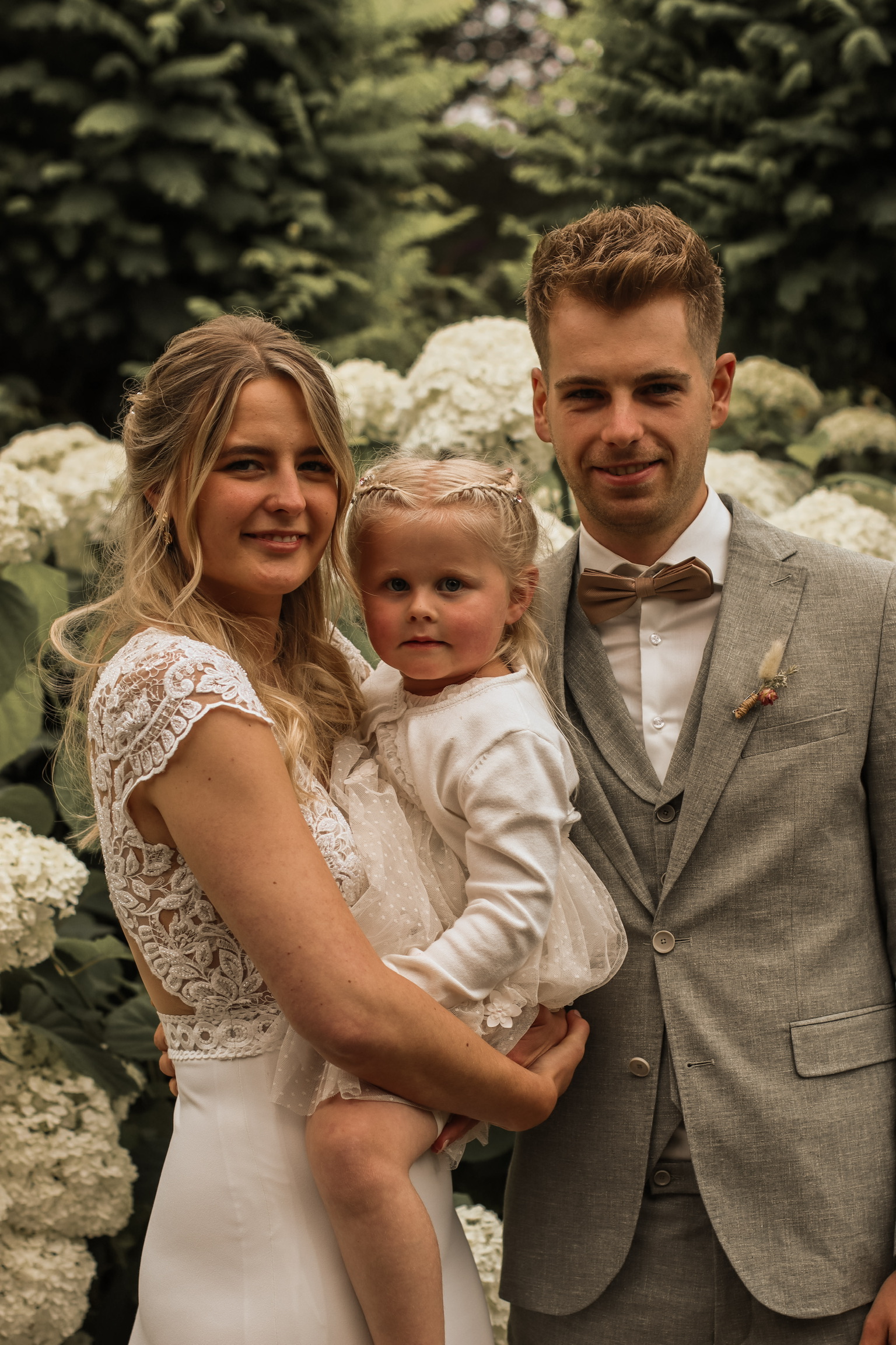 Bruiloft fotografie Haaksbergen - bruidspaar met kind tussen witte bloemen door Kim Scharenborg Fotografie