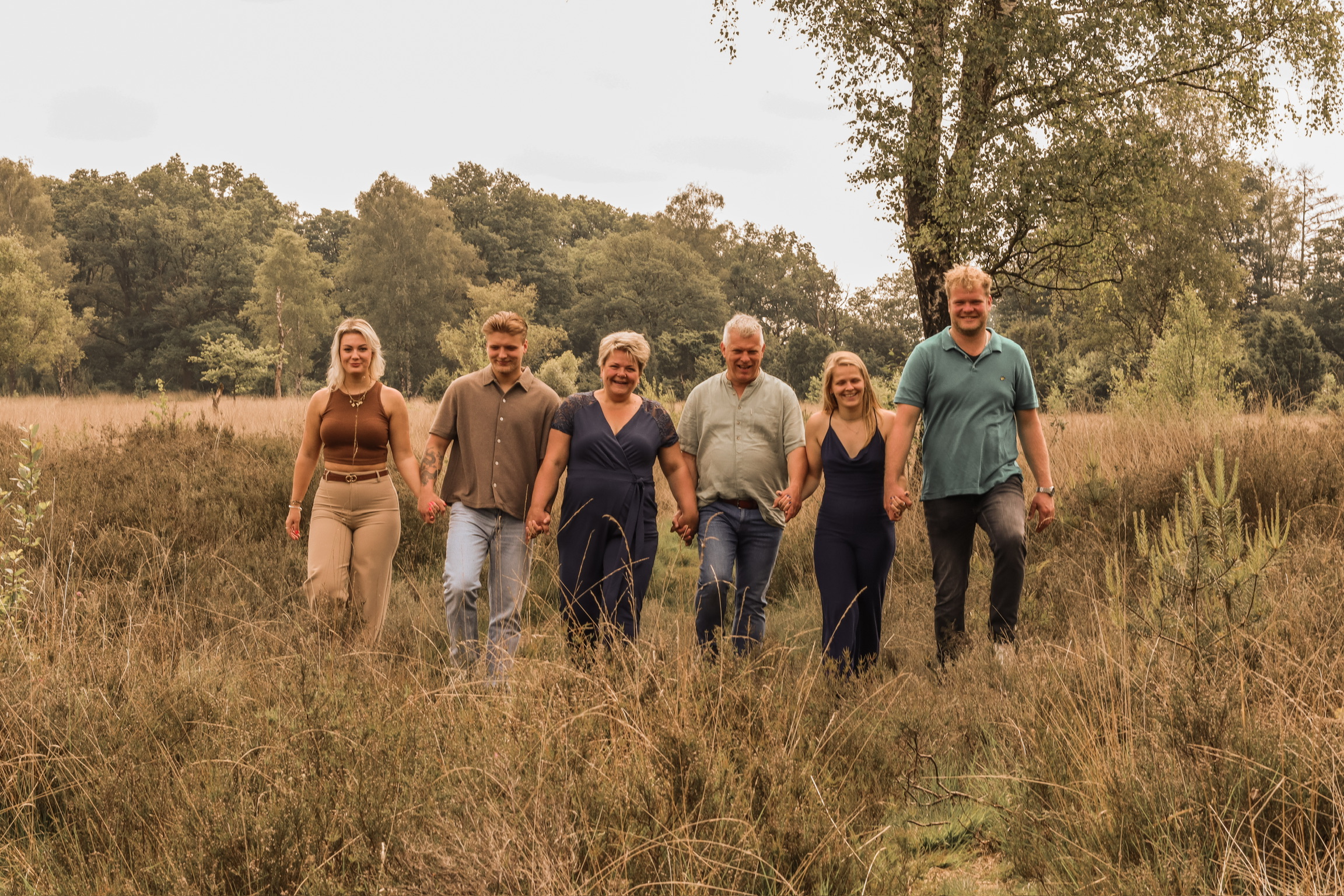 Familie fotografie Haaksbergen - grote familie van zes personen hand in hand in gouden grasveld door Kim Scharenborg Fotografie