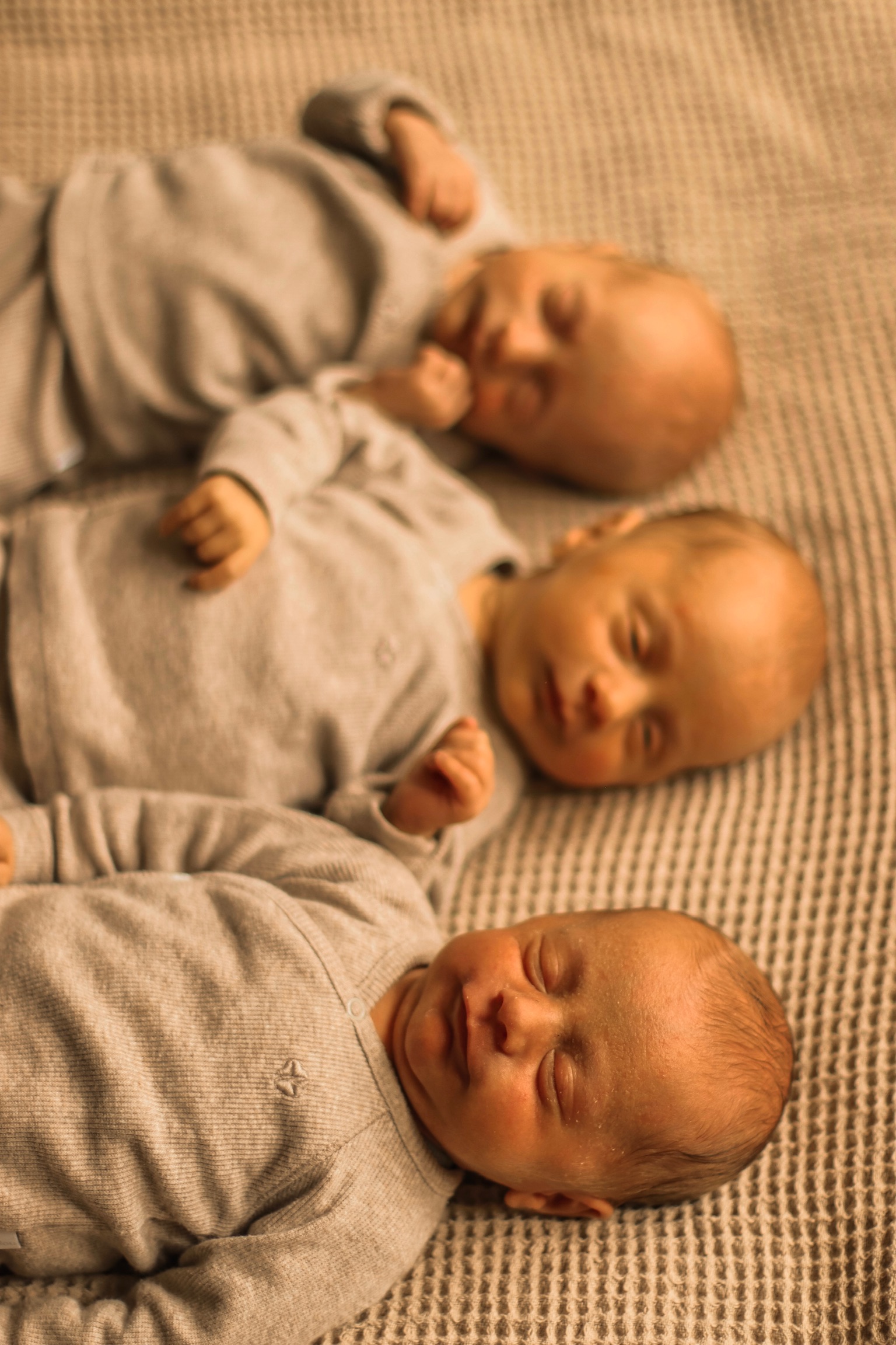 Newborn fotografie Haaksbergen - drie pasgeboren baby's in beige rompertjes op gestreepte deken door Kim Scharenborg Fotografie