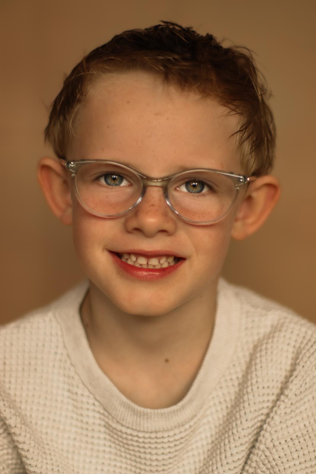 Portret fotografie Haaksbergen - jongen met bril op beige achtergrond door Kim Scharenborg Fotografie